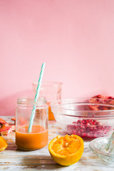 Pomegranate and orange juice on a jar glass with a fnnel juice. Fruts pomegranate seeds and orange cut in half around,top view over a wooden background, against a pink    background