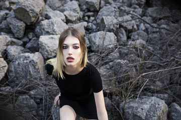 Girl model in a black T-shirt posing against a background of stones