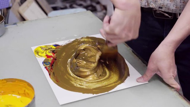man mixes paint until golden in color, being ruled by the printing press machine and print company's logo on packaging products