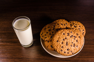 Plate with chocolate chip cookies and a glass of milk on a dark wooden table