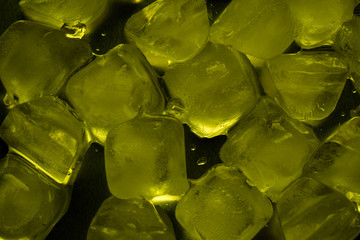 Ice cubes in yellow on a reflecting table with ice drops