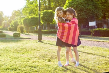 Two little girl friends schoolgirl 7-8 years embracing playing on the meadow in the park.