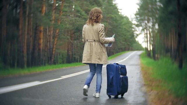 Young beautiful woman hitchhiking standing on the road with a suitcase on a table with an inscription SEA