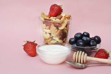 Healthy Breakfast with Oat Flakes, Natural Yogurt, Fresh Blueberries, Strawberries, Almonds and Honey in Glass Bowls. Flat Lay. Pink Background.