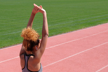 Sports exercises and stretching or preparing a runner to start at the stadium. A young beautiful dark-skinned girl in a gray tank top raised her arms and stood on the treadmill. View from the back.