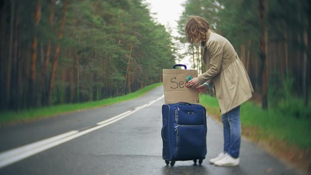 Young beautiful woman hitchhiking standing on the road with a suitcase on a table with an inscription SEA