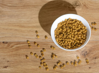 It is the glass full bowl with a dry natural cat food. The granulated pet mix is scattered on a floor.