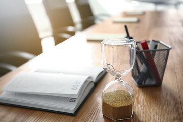 Fototapeta na wymiar Notebook, hourglass and pencil holder on table indoors. Business meeting in conference hall