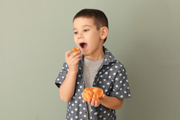 Funny little boy eating citrus fruit on color background