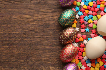 Composition with chocolate Easter eggs, colorful sprinkles and candies on wooden background