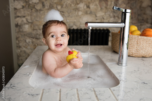 Baby Taking Bubble Bath In Kitchen Sink Holding Rubber Duck