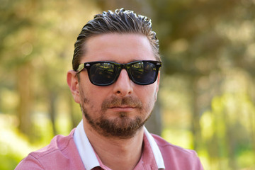 Young man's outdoors portrait looking at the camera who has sunglasses with natural green background. Neutral, happy, sad, disgust, fear, surprise Facial Emotion.