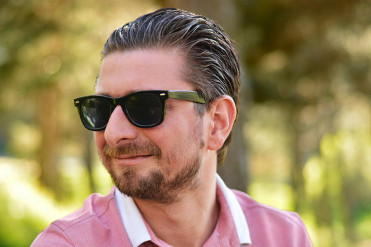 Young man's outdoors portrait looking at the camera who has sunglasses with natural green background. Neutral, happy, sad, disgust, fear, surprise Facial Emotion.