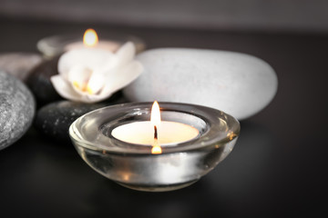 Obraz na płótnie Canvas Burning candle and spa stones on black table