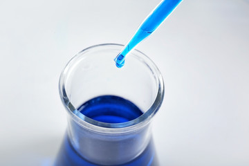 Dripping blue liquid into flask on light background