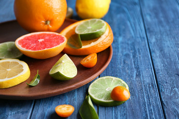 Plate with fresh citrus fruits on wooden table