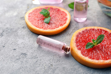 Bottle of essential oil and citrus slices on table, closeup