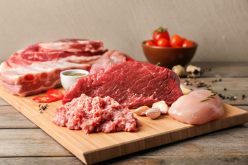 Wooden board with different kinds of raw meat on table