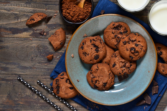 Homemade chocolate cookies in a plate with milk on a wood background.