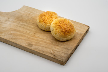 Two whole buns with sesame seeds on wooden square cutting board isolated on white