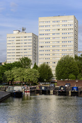 Typical high rise apartment block, located in an English city. The building is located overlooking a canal, which has canal boats moored at the bank. The weather is sunny