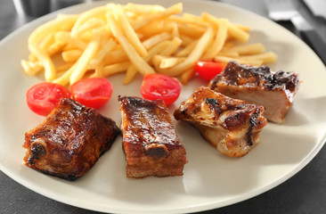 Delicious grilled ribs and french fries on plate, closeup