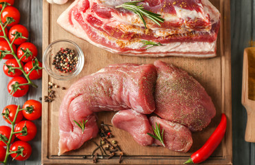 Wooden board with fresh pork meat and spices on grey table