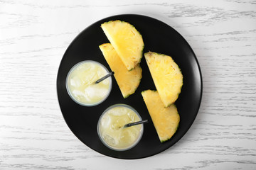 Plate with sliced pineapple and glasses of fresh juice on white wooden table