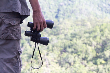 Young male hiker hand holding binoculars  relaxing on top of a mountain - Holiday activities. - Pictures with space for editing.