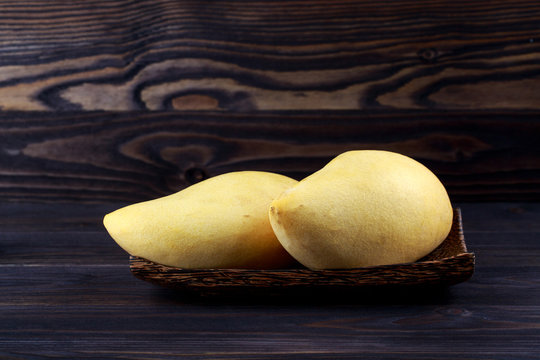 Whole fruits of yellow mango in wooden plate on dark background