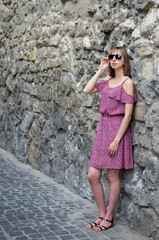 Graceful stylish young woman in red dress and sunglasses gladly posing while walk outside in good mood, street style. Outdoor close-up photo pleased girl in trendy summer dress, 