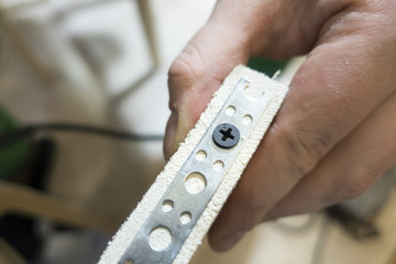 Mounting mounting perforated tape close-up on a wooden board and swirling screw