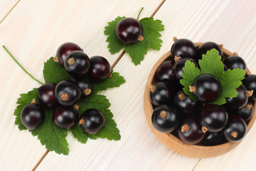 black currant in wooden bowl with green leaf on white wooden background. top view