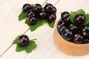 black currant in wooden bowl with green leaf on white wooden background. top view