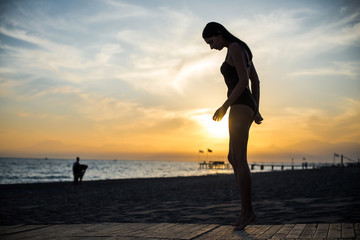 beautiful tan woman in bikini walking on the beach admiring sunset