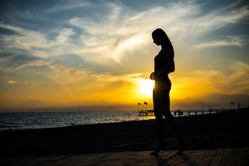 beautiful tan woman in bikini walking on the beach admiring sunset