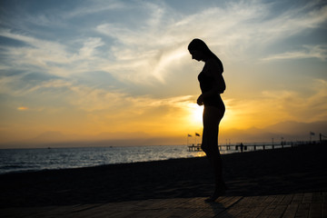 beautiful tan woman in bikini walking on the beach admiring sunset