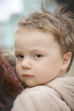 Portrait of a child boy in the arms of a mother with a serious face close-up.