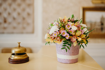 Service bell and flowers on wood reception board with blurred hotel background.