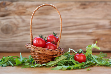 cherry tomatoes and arugula leaves in a small basket on a wooden background