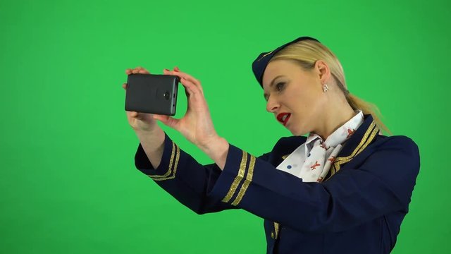 A young beautiful stewardess takes pictures with a smartphone - green screen studio