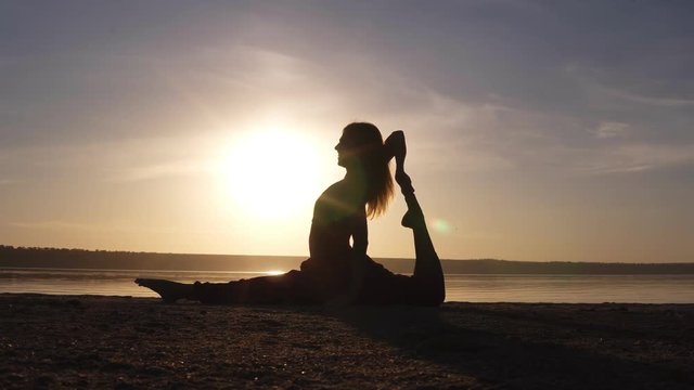 Young pretty woman wearing yoga sportswear working out against sea, doing yoga or pilates exercise. Variation of monkey god, splits, hanumanasana with backbend. Full length