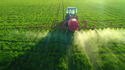 Aerial view of farming tractor plowing and spraying on field - Powered by Adobe
