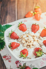 Oatmeal with cottage cheese, peanut and strawberries on wooden background. Summer healthy breakfast.