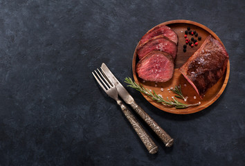 Roast beef on a wooden plate with spices and rosemary, on a concrete background black background,...