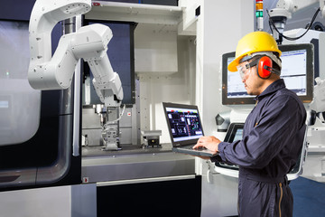 Maintenance engineer using laptop computer control automatic robotic hand with CNC machine in smart factory, Industry 4.0 concept