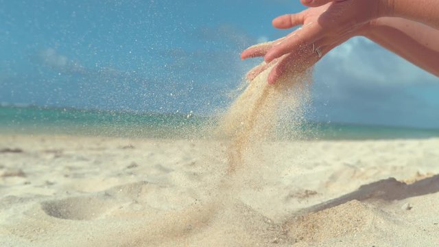 SLOW MOTION, CLOSE UP, COPY SPACE: Coarse white sand slips between unrecognizable girl's soft fingertips and onto the paradise island beach. Cheerful woman playing with sand during summer vacation.