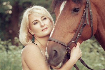 Beautiful sexy woman rider blonde in light air dress kisses walks in the woods with a horse