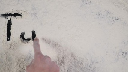 finger write TUESDAY on a white flour background. top view 4k