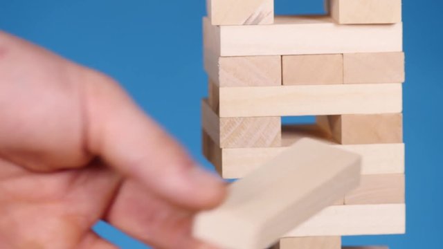 hands of Young man plays jenga on blue background, close-up. A man builds a tower of blocks while playing jenga